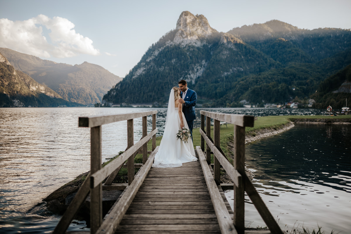 Brautpaar das auf einer Brücke am Traunsee in Traunkirchen steht, mit dem Kleinen Sonnstein im Hintergrund, fotografiert von Hochzeitsfotograf Kosia aus Grieskirchen in Oberösterreich
