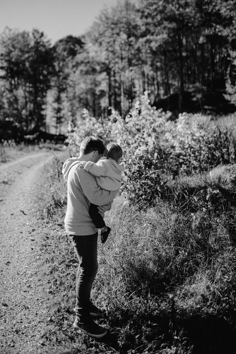 Schwarz-weiß Foto eines Jungen mit einem Baby am Arm, fotografiert von Familienfotograf Kosia - die wunderschöne Aussicht diente als Kulisse für Familienfotos am Almsee