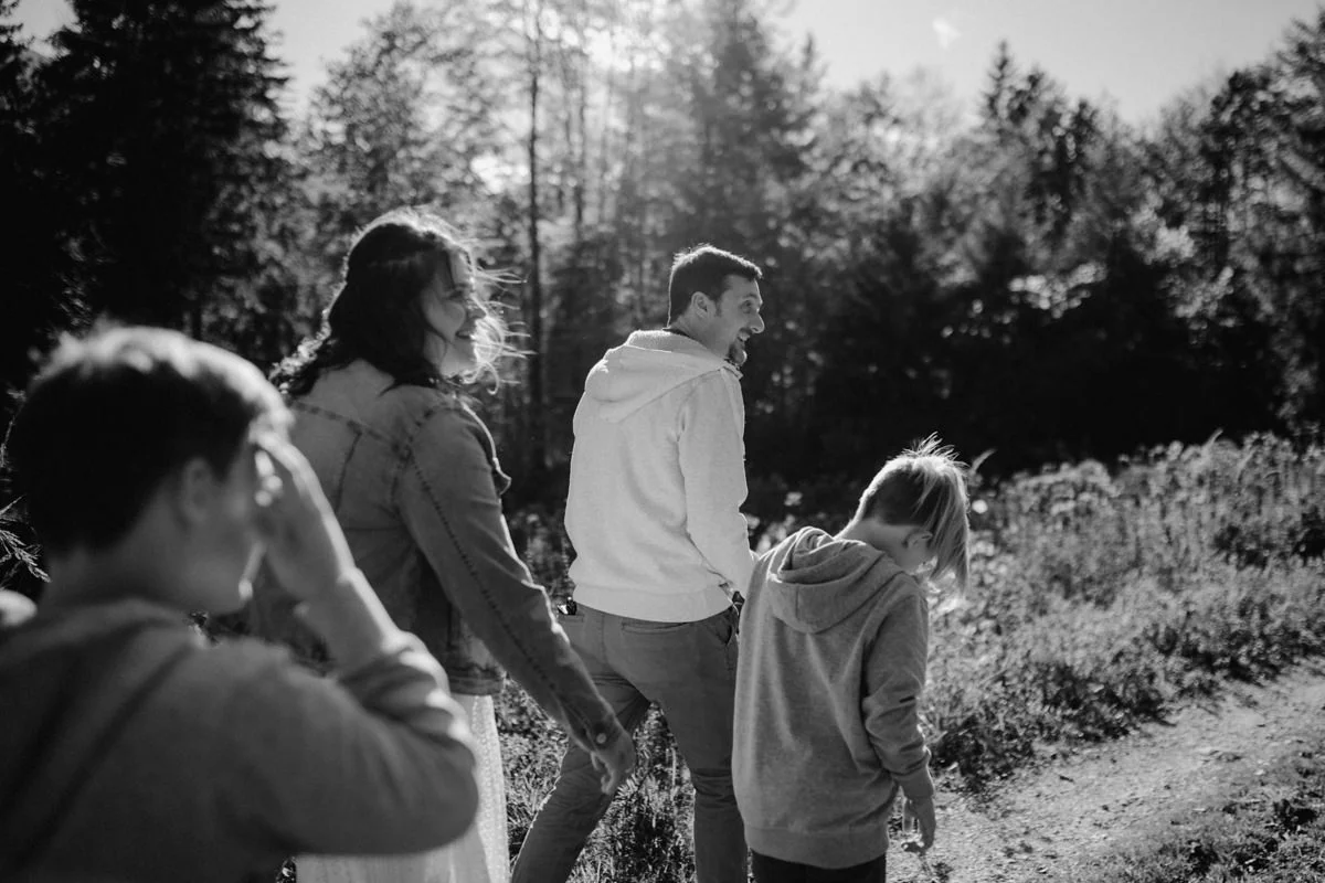 Schwarz-weiß Foto einer Familie, die lachend einen Feldweg in der Nähe des Almsee entlang geht, fotografiert von Familienfotograf Kosia - die wunderschöne Aussicht diente als Kulisse für Familienfotos am See