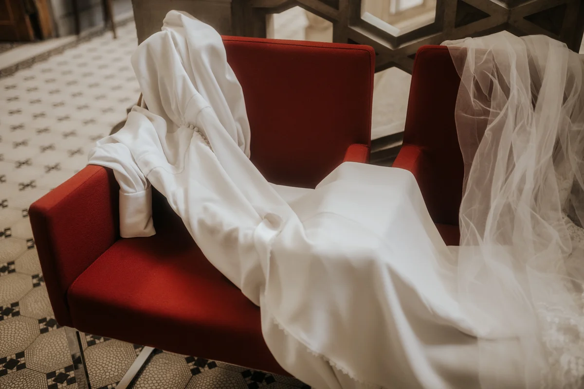 Detailfoto eines Hochzeitskleides von Atelier Bona Res, das auf einem roten Stuhl liegt, fotografiert von Hochzeitsfotograf Kosia bei einem Hochzeit-Shooting in Wels