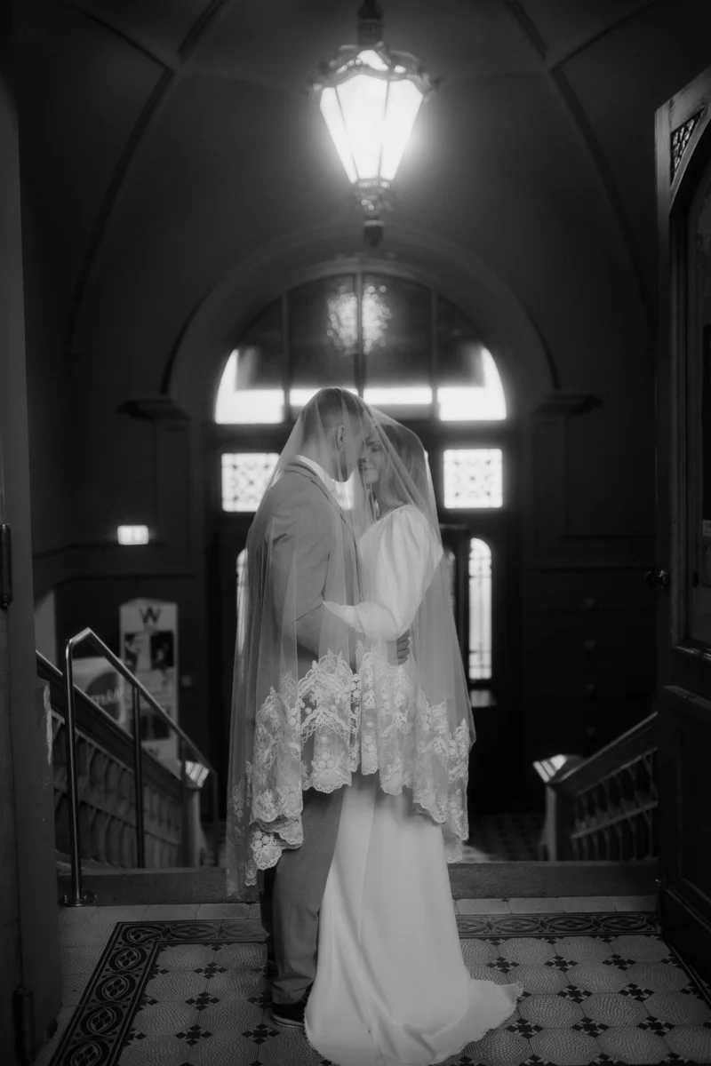 Brautpaar das von einem Schleier umhüllt in der Eingangshalle des Medienkulturhauses steht, fotografiert bei einem Hochzeit-Shooting in Wels