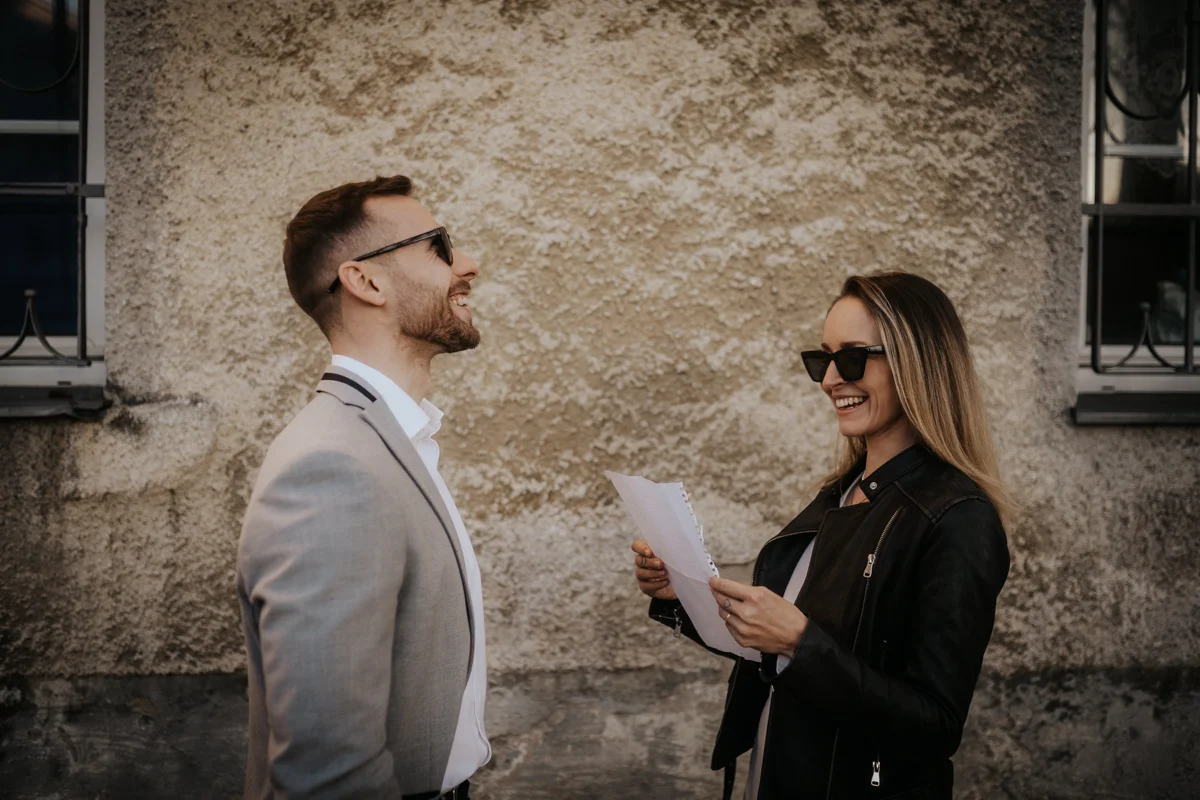 Lachendes Brautpaar, das sich vor einem alten Gebäude gegenseitig einen Liebesbrief vorliest, fotografiert bei einem Hochzeit-Shooting in Wels