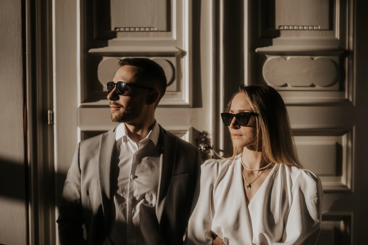 Brautpaar mit Sonnenbrillen im direkten Sonnenlicht, das vor einer Tür im Medienkulturhaus steht. Fotografiert von Hochzeitsfotografin Kosia bei einem Hochzeit-Shooting.