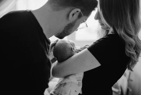 Schwarz-weiß Foto von frischgebackenen Eltern, die ihr Neugeborenes im Arm halten. Fotografiert bei einem Newborn Shooting in Oberösterreich, von Fotograf Kosia