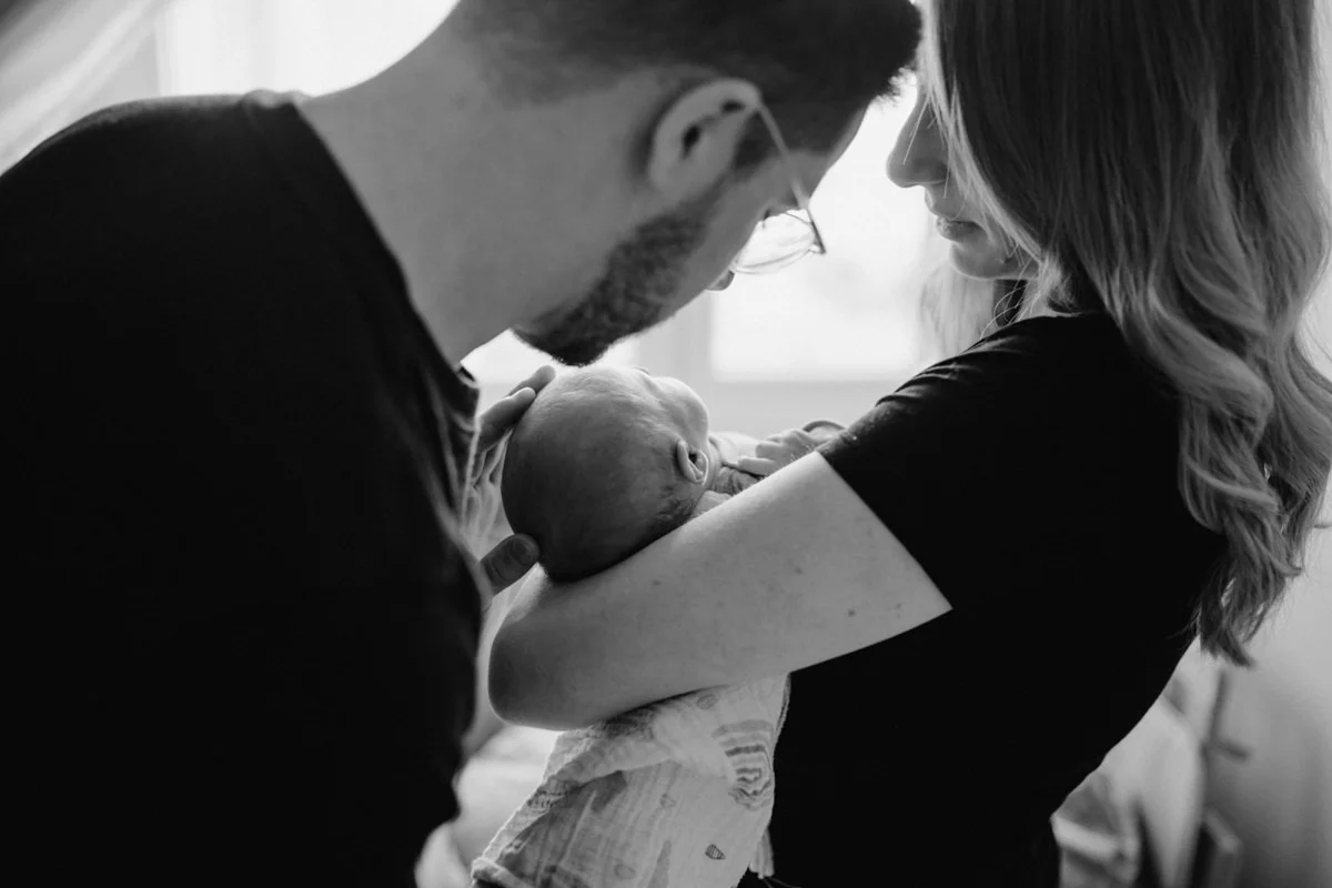 Schwarz-weiß Foto von frischgebackenen Eltern, die ihr Neugeborenes im Arm halten. Fotografiert bei einem Newborn Shooting in Oberösterreich, von Fotograf Kosia