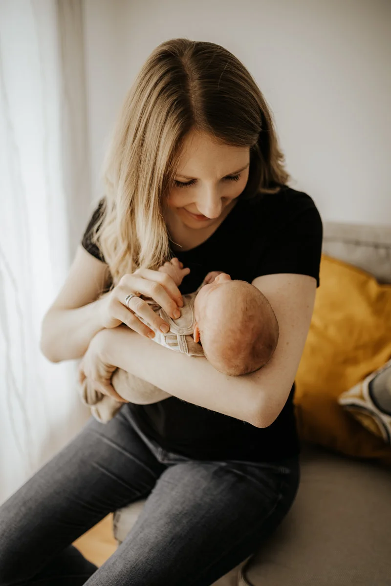 Mutter die ihr neugeborenes Baby am Arm hält und ansieht, fotografiert von Fotograf Kosia bei einem Newborn-Shooting in Oberösterreich