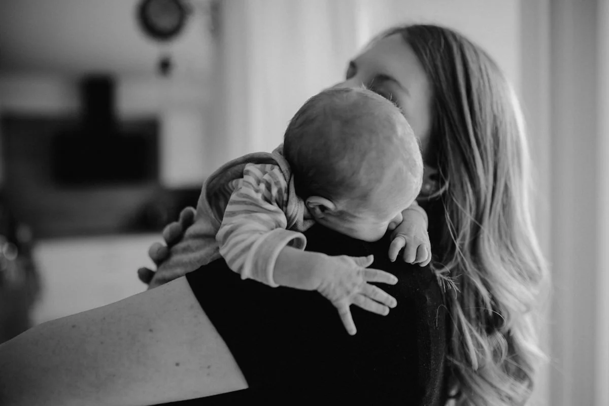 Schwarz-weiß Foto einer Mutter, die ihr Neugeborenes am Arm hält, fotografiert von Fotograf Kosia bei einem Newborn-Shooting in Oberösterreich