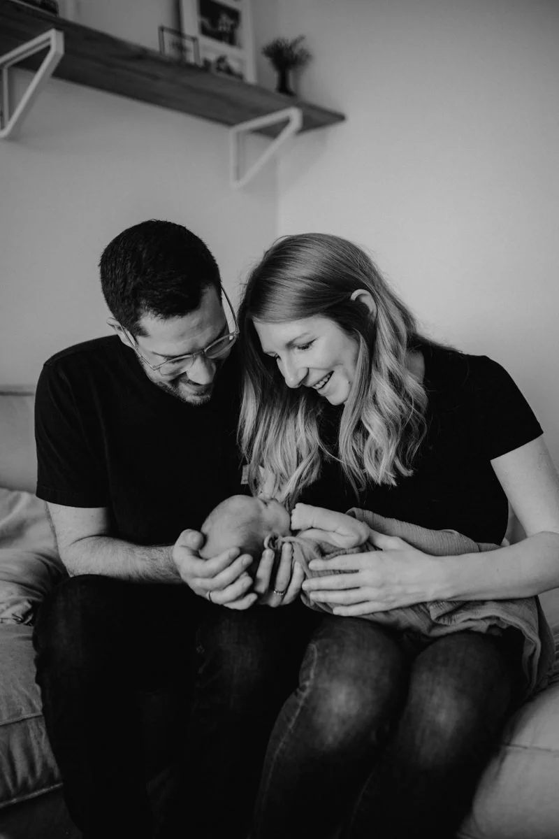 Schwarz-weiß Foto von Eltern, die ihr neugeborenes Baby im Arm halten, fotografiert von Fotograf Kosia bei einem Newborn-Shooting in Oberösterreich