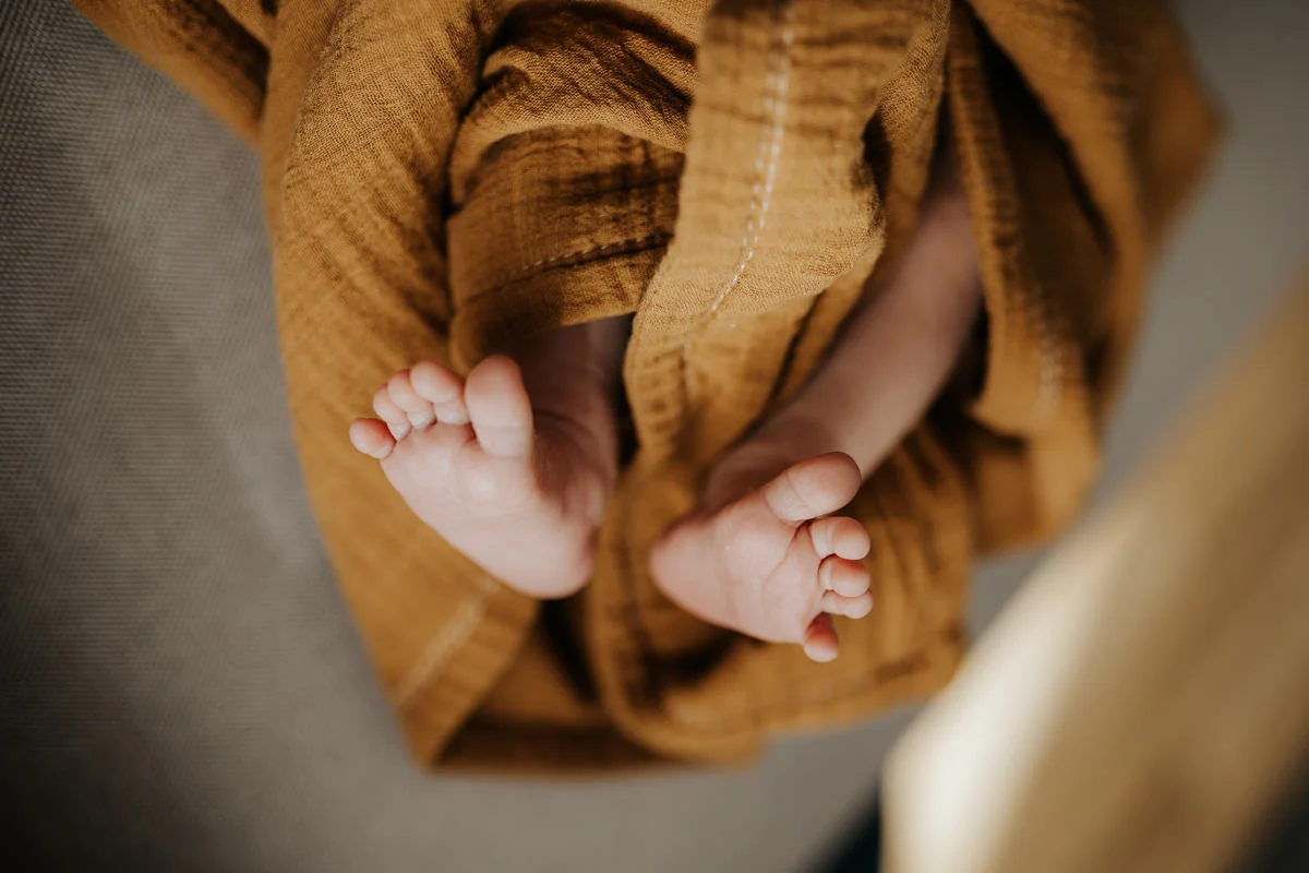 Detail-Foto von Füßen eines kleinen Neugeborenen, die in eine senf-farbene Decke gewickelt sind, fotografiert von Fotograf Kosia bei einem Newborn-Shooting in Oberösterreich