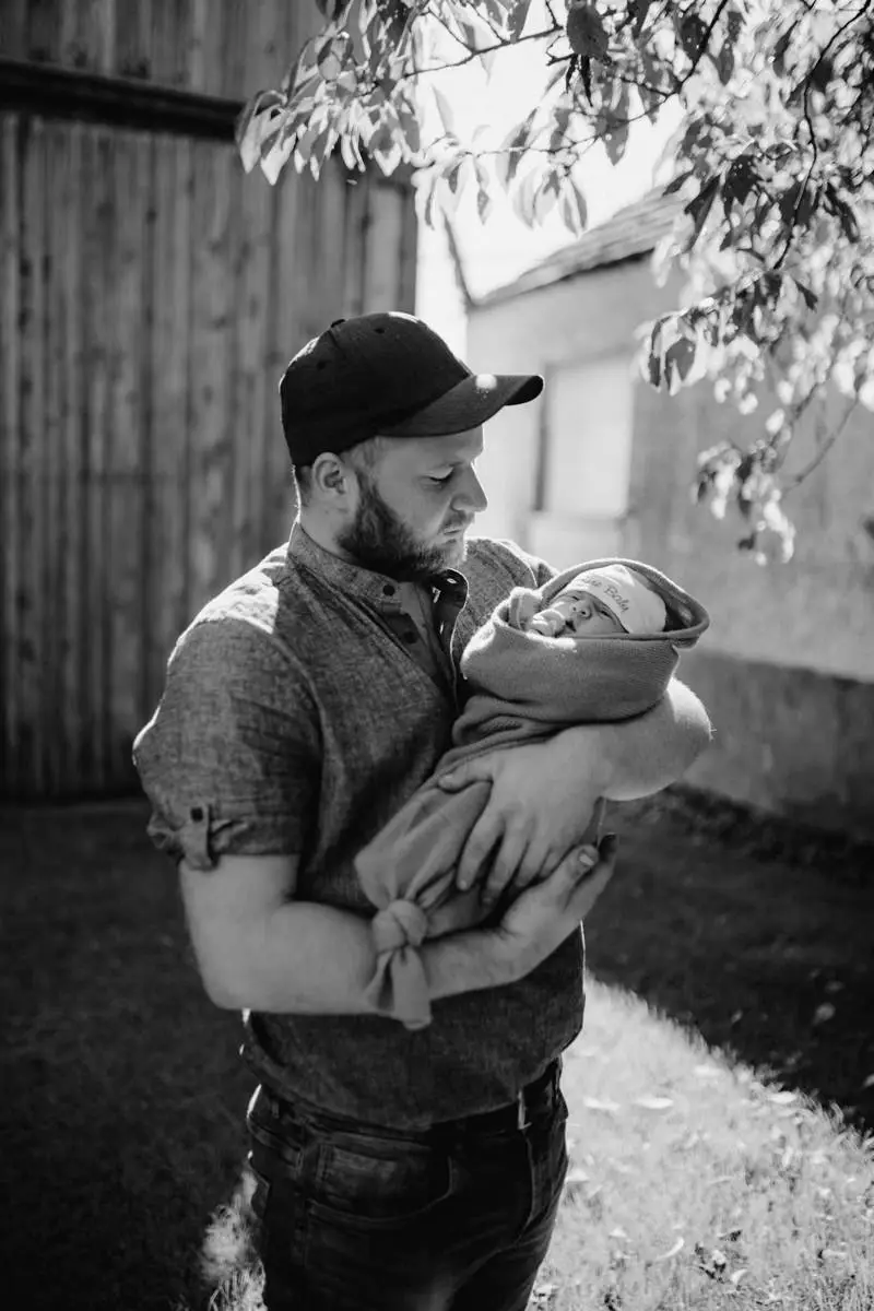 Schwarz-Weiß-Foto von einem Vater, der seine neugeborene Tochter am Arm hält, bei einem Newborn Shooting in Ried, fotografiert von Fotograf Kosia