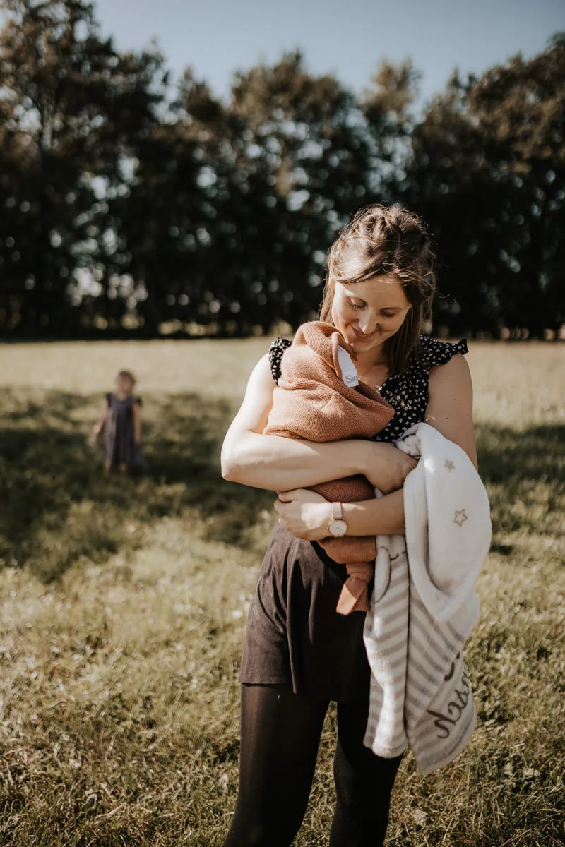 Eine Mutter hält ihr Neugeborenes in eine Decke eingewickelt in der Hand, bei einem Newborn Shooting in Ried fotografiert von Fotograf Kosia