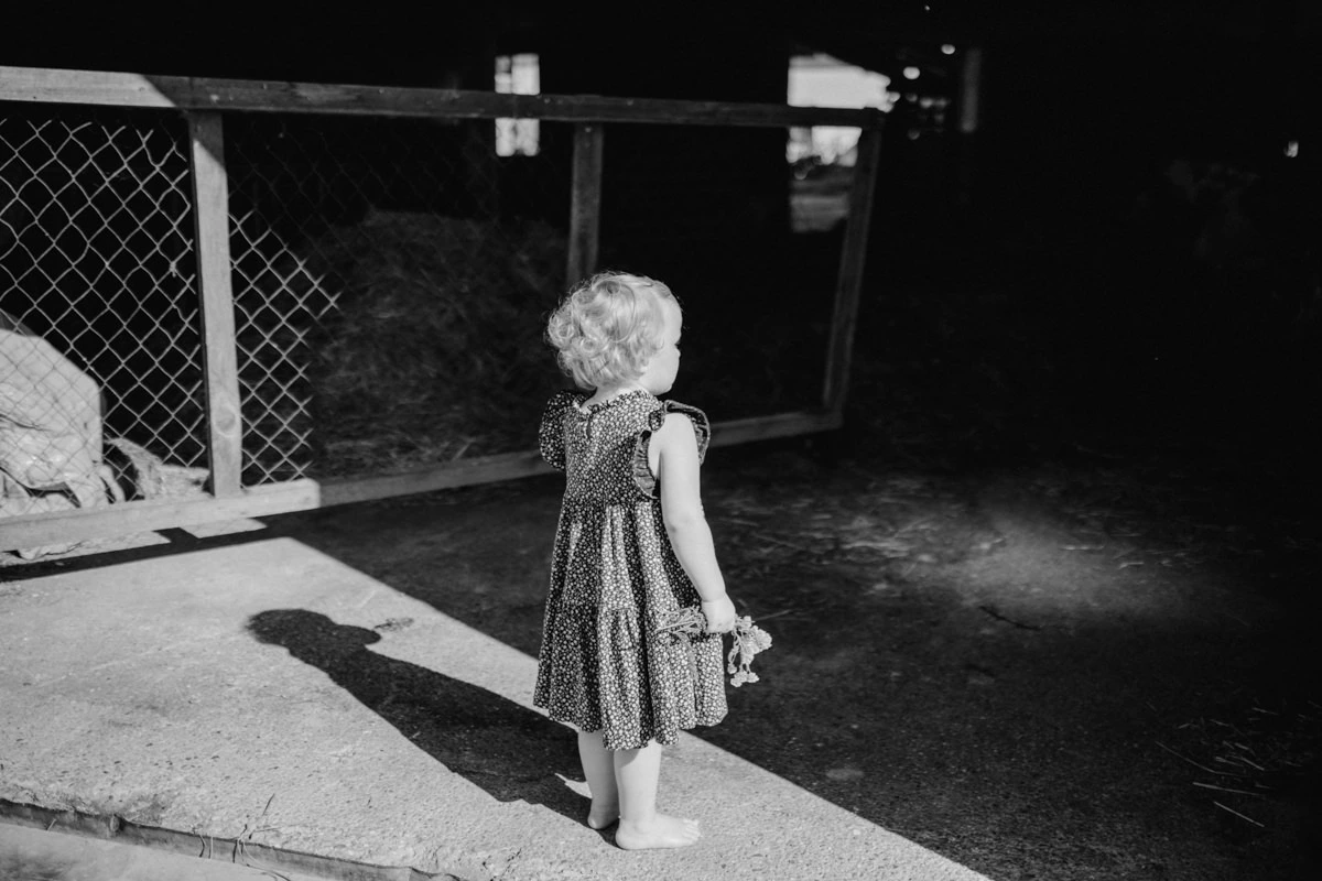 Mädchen das mit Blumen in der Hand vor einem Stall steht, bei einem Newborn Shooting in Ried fotografiert von Fotograf Kosia